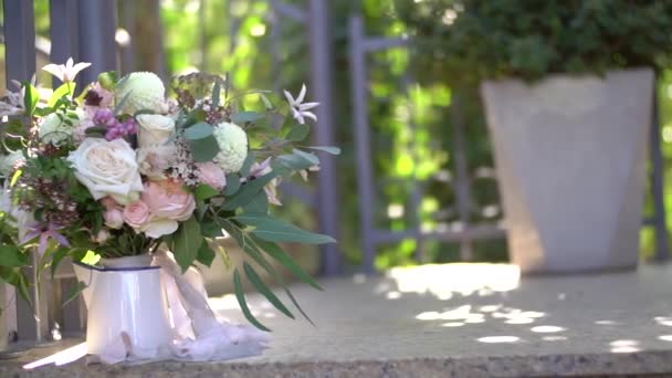 Strauss aus rosa und cremefarbenen Rosen, Eukalyptuszweigen, weißen Dahlien und zarten lila Blüten in einer weißen Vase am geschmiedeten Gitter — Stockvideo