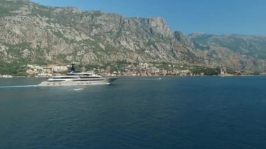 Yat, Kotor Körfezi boyunca ilerliyor. Arkasında güzel dağlar ve rahat küçük bir kasaba var.