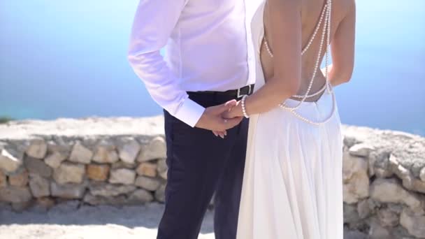 Наречений і наречена в незвичайній весільній сукні з відкритою спиною тримають руки — стокове відео