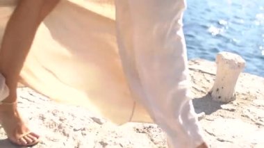 Beyaz elbiseli bir gelin iskelede yürüyor, etekleri rüzgarda dalgalanıyor. 