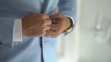 Bir adam hazırlanıyor ve ceketinin düğmelerini ilikliyor.