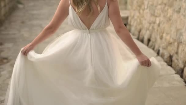 Η νύφη με ένα ντελικάτο φόρεμα γυρίζει στο δρόμο της παλιάς πόλης, κρατώντας τη φούστα της — Αρχείο Βίντεο