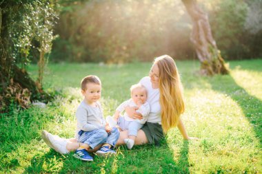 Annem iki çocuğuyla çimenlerde oturuyor.