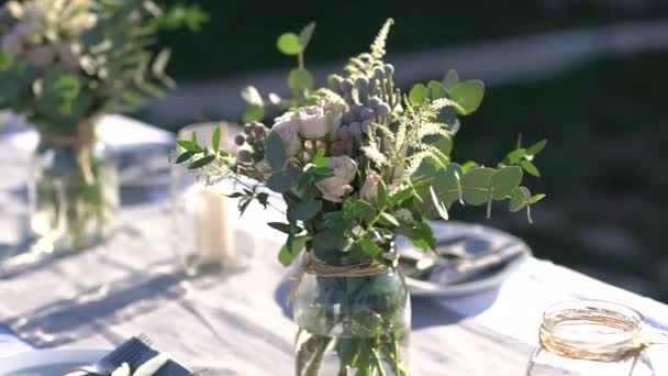 Μπουκέτα με τριαντάφυλλα, αστίλβα, κορταδέρια και κλαδιά ευκαλύπτου σε βαζάκια σε γιορτινό τραπέζι κατά τη διάρκεια γαμήλιας δεξίωσης — Αρχείο Βίντεο