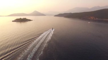 Mamula Adası 'nın arka planında seyreden bir motorlu tekne, Kotor Körfezi' nde dağlar ve resimli yamaçlar. 