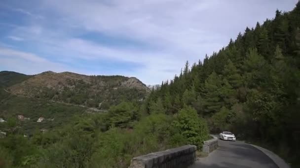 Ein weißes Cabrio fährt die schöne grüne Bergstraße in Montenegro entlang — Stockvideo