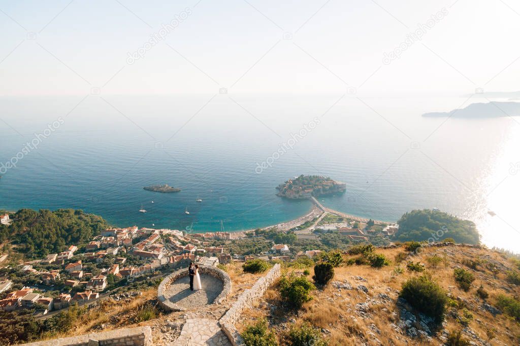 The bride and groom embrace on the observation deck in front of them a panoramic view of the sea and the island of Sveti Stefan 