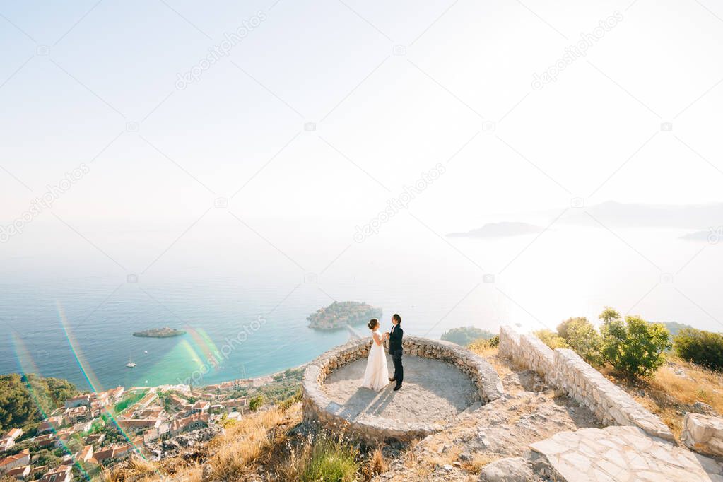 The bride and groom embrace on the observation deck overlooking the island of Sveti Stefan 