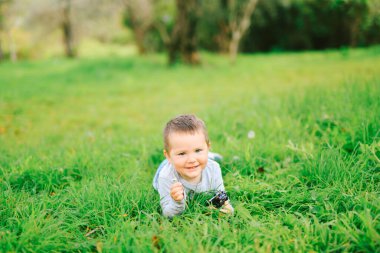 Parktaki çimlerin üzerinde karnının üzerine uzanmış şirin bir çocuk.