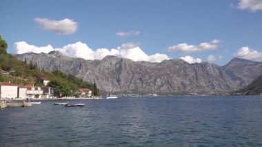 A boat sails in the middle of the Bay of Kotor, in front of it is a mount near the cozy town