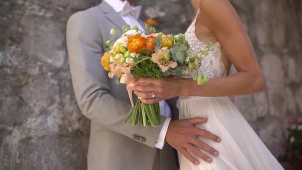 The bride and groom are embracing at the stone wall of an old house, close-up — Video Stock