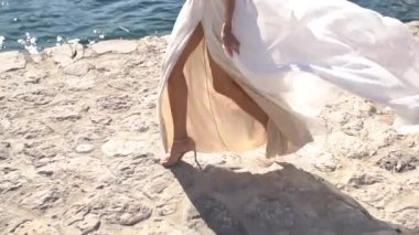 Beyaz elbiseli bir gelin iskelede yürüyor, etekleri rüzgarda dalgalanıyor. 