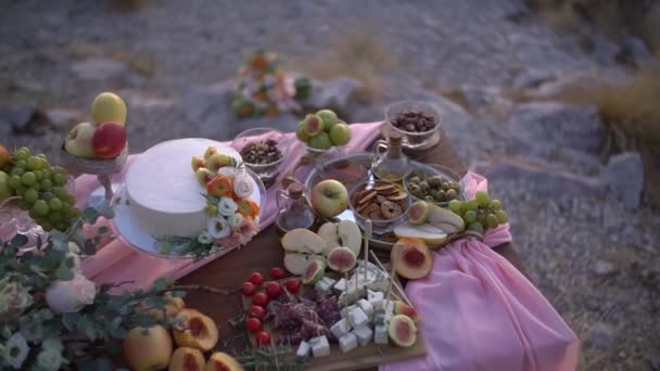 Mesa buffet de casamento com lanches, frutas, bolo decorado com pano rosa, flores e um candelabro com velas — Vídeo de Stock