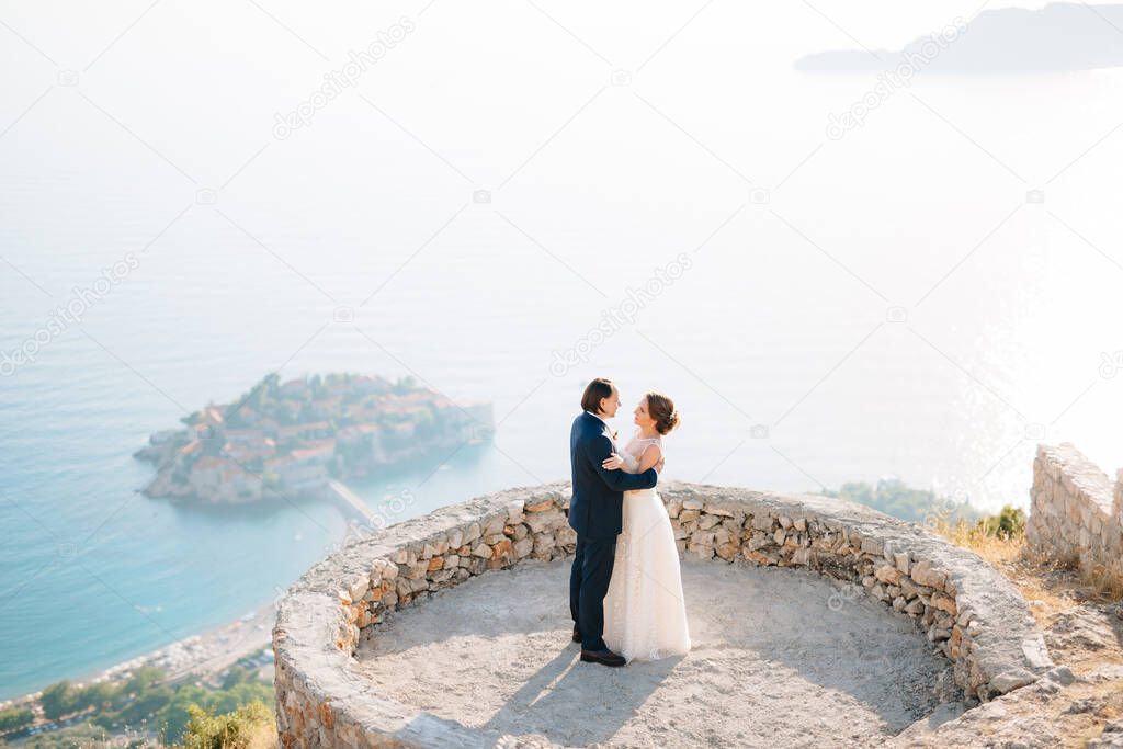 The bride and groom embrace on the observation deck overlooking the island of Sveti Stefan 