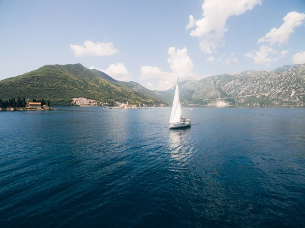 A white sailing yacht sails along the Bay of Kotor with the islands in the background near Perast in Montenegro.
