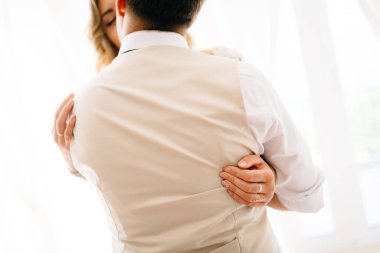 Gelin damadı sıkıca kucaklıyor, damat onu öpüyor, damadın arkasından manzara. 