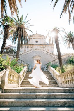 Gelinlik giymiş bir gelin Prcanj 'da eski bir tapınağın merdivenlerinde dönüyor, eteği rüzgarda sallanıyor. 