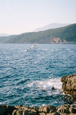 Güneşli bir günde, beyaz bir yat. Resimli sahillerin yakınında, dağların arka planında..