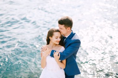 Damat, gelini deniz kıyısında omuzlarından kucaklıyor. 