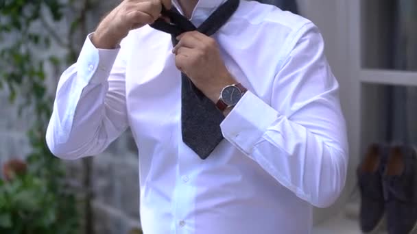 Um homem de camisa branca amarra um laço enquanto se prepara para uma cerimônia de casamento — Vídeo de Stock
