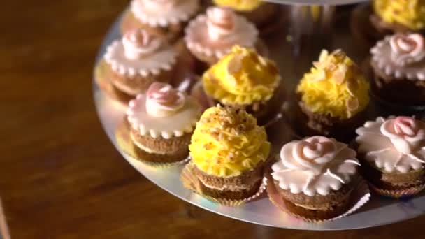 Stand met cupcakes versierd met gele en roze crème op een feestelijk banket — Stockvideo