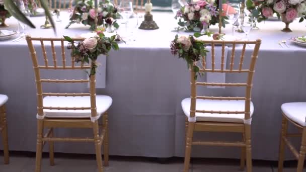 Stoelen bij de tafel bij een bruiloftsbanket, versierd met bloemen en kandelaars met brandende kaarsen op de pier aan zee — Stockvideo