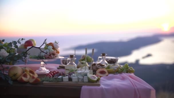 Ślubny stół bufetowy z przekąskami, owocami, tortem ozdobionym różową szmatką, kwiatami i świecami z widokiem na Zatokę Kotor — Wideo stockowe