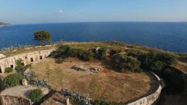 Mamula kalesinin üst manzarası, kayalık kıyı, üzerinde uçan martılar ve deniz ufku. 