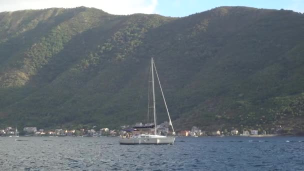 Kotor Körfezi 'nin ortasında bir yat yelken açar. Önünde sıcak kasabanın yakınında bir dağ vardır. — Stok video