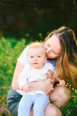 Anne çimenlerde otururken bebeğini öpüyor.