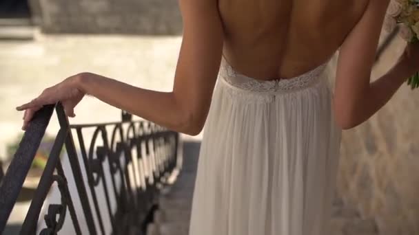 Panna młoda w pięknej sukience z otwartym tyłem schodzi po schodach, widok z tyłu — Wideo stockowe