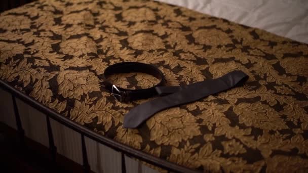 Δερμάτινη ζώνη και γραβάτα ξαπλώνουν στο κρεβάτι του ξενοδοχείου κατά την προετοιμασία της τελετής του γάμου — Αρχείο Βίντεο