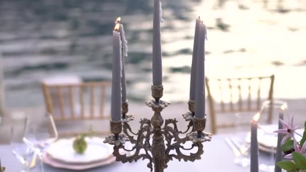 Урожай канделябр з палаючими свічками стоїть на столі з столовими приборами під час весільного бенкету біля моря — стокове відео