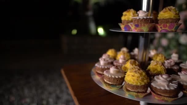 Stand com cupcakes decorados com creme amarelo e rosa em um banquete festivo — Vídeo de Stock