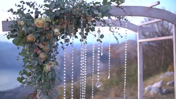 Белая деревянная свадебная арка, украшенная розами, эвкалиптом и хрустальными подвесками, крупным планом — стоковое видео