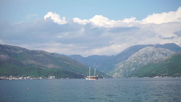 Eine Jacht segelt mitten in der Bucht von Kotor, davor liegt ein Berg in der Nähe der gemütlichen Stadt — Stockvideo
