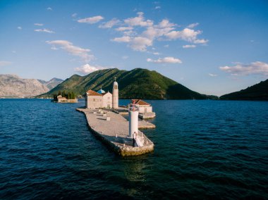 Gelin ve damat, Kayalıkların Hanımefendisi adasındaki iskelede fenerin yanında durup öpüşüyorlar. 