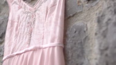 Taş duvarda asılı soluk pembe bir gelinliğin boncuklu korsesi, yakın plan.