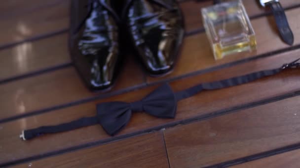 Lacquered mens shoes, wrist watch, perfume, cufflinks, bow tie on wooden background — Stock Video