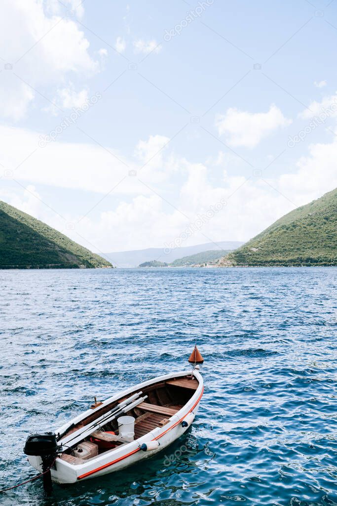 A white fishing boat sways on the water against the backdrop of the picturesque countryside of Perast.