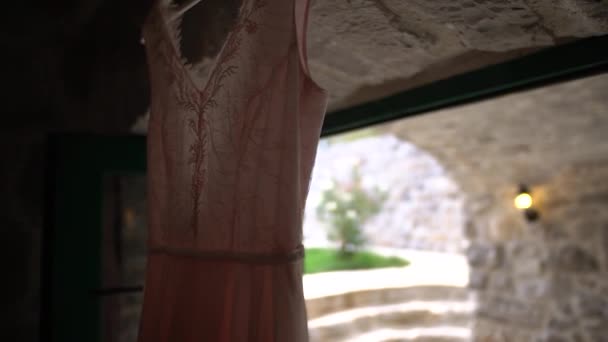 Un hermoso vestido de novia de color rosa pálido cuelga por encima de la entrada de una acogedora habitación con puertas verdes — Vídeos de Stock