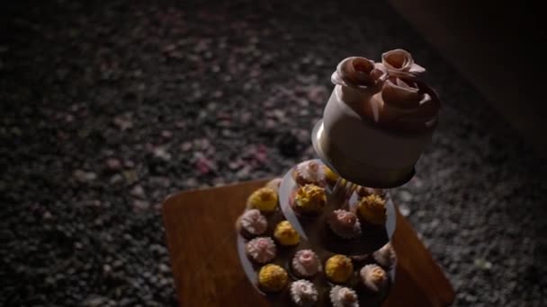 Stand com cupcakes decorados com creme amarelo e rosa e bolo pastel com rosas creme em um banquete festivo — Vídeo de Stock