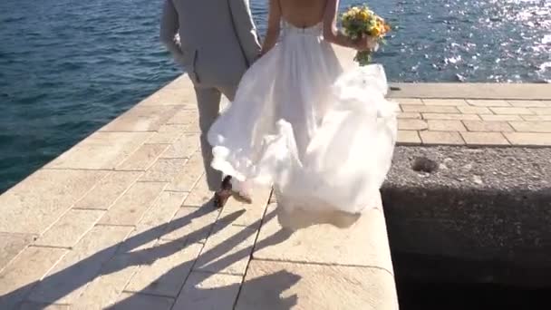 Bruden och brudgummen går på piren, bruden kramar buketten. — Stockvideo