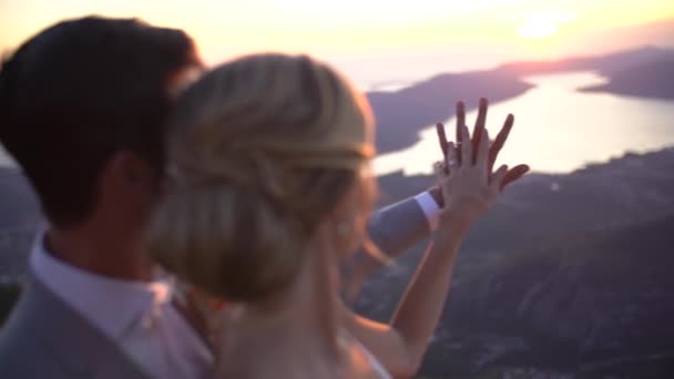 La novia y el novio están abrazando y viendo la puesta de sol sobre la bahía de Kotor, la novia puso su mano en la mano de los novios — Vídeo de stock