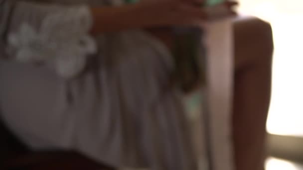 Женщина в шелковом халате держит на коленях свадебный букет и играет с длинными лентами — стоковое видео
