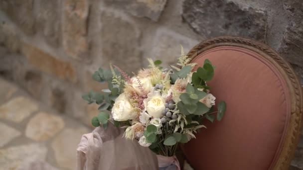 Delicate bridal bouquet and delicate fabric in a pink armchair against a stone wall — Stock Video