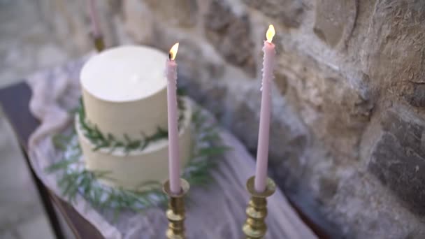 Gâteau à la crème blanche, décoré de branches d'olivier et d'eucalyptus, à côté des bougies ardentes en chandeliers dorés — Video