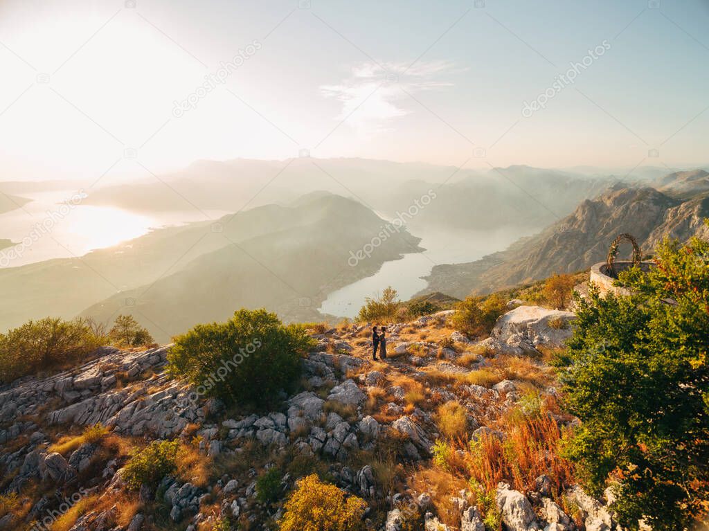 The bride and groom embracing on the Lovcen mountain behind them opens a view of the Bay of Kotor 