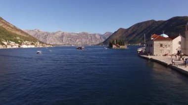 Kotor Körfezi 'ndeki Rocks Adası' nın rıhtımındaki turist teknesinde insanlar kilisenin yanında yürür. 