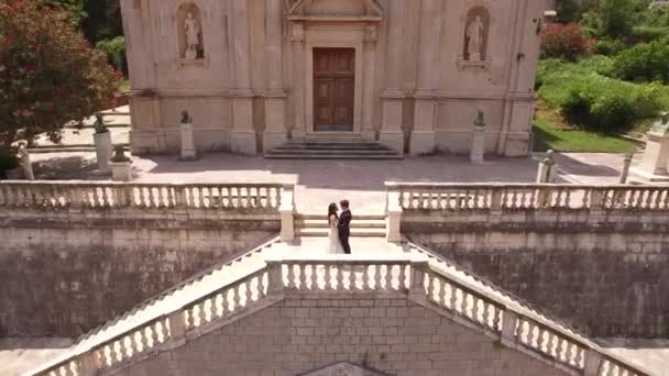 The bride and groom stand hugging on the ancient stairs of the Nativity of the Blessed Virgin Mary church — Stock Video